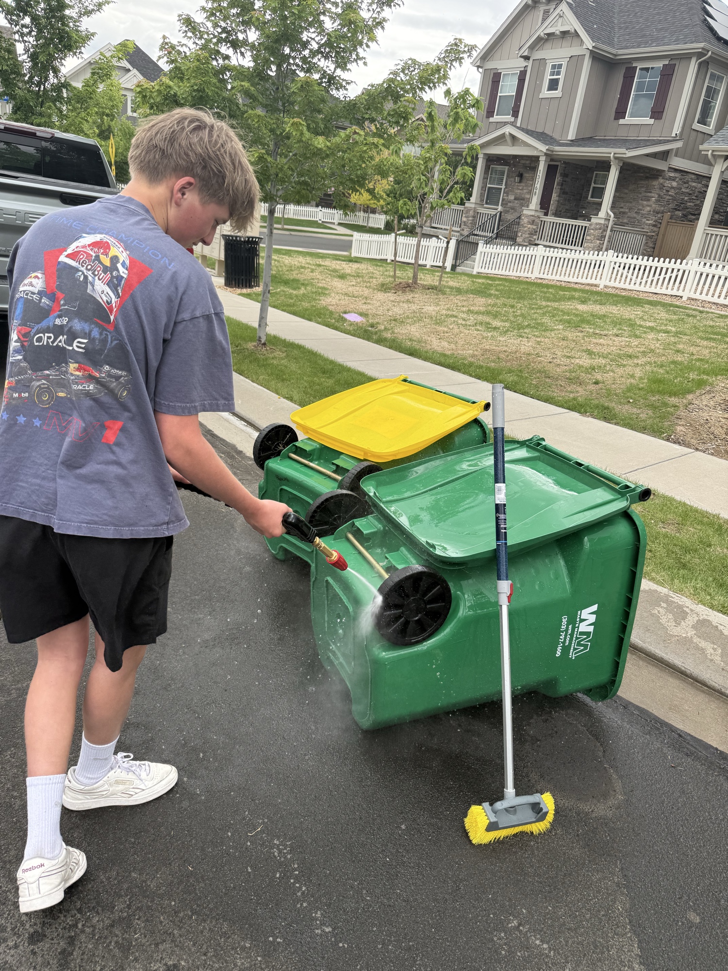 Jack pressure washing the outside of a green trash bin at the curb