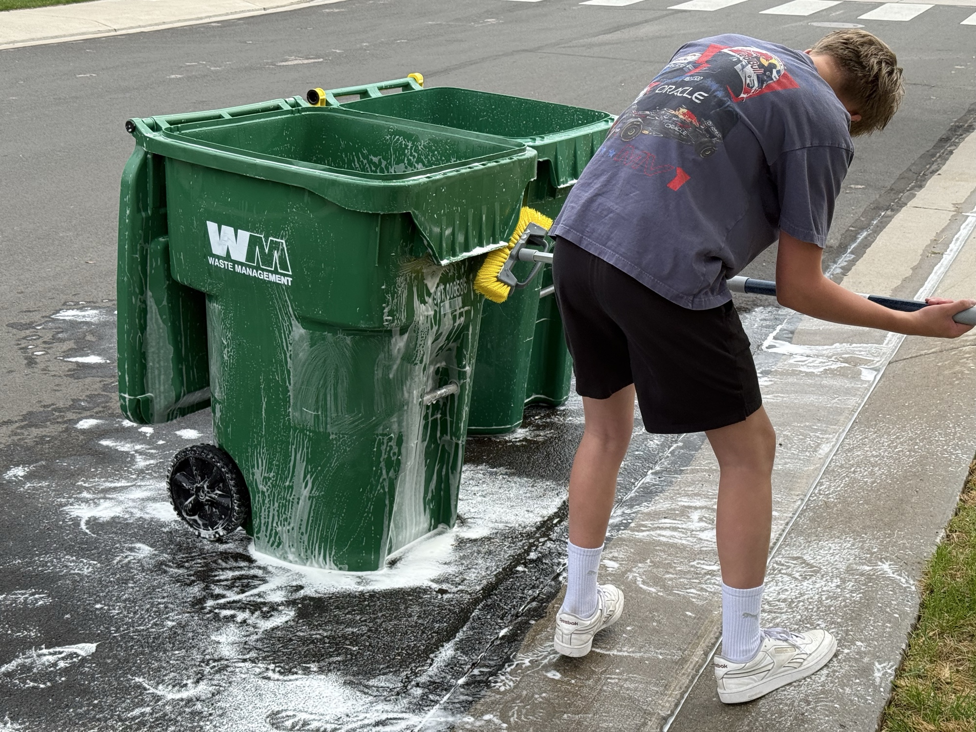 Jack scrubbing the outside of a green trash bin with a brush
